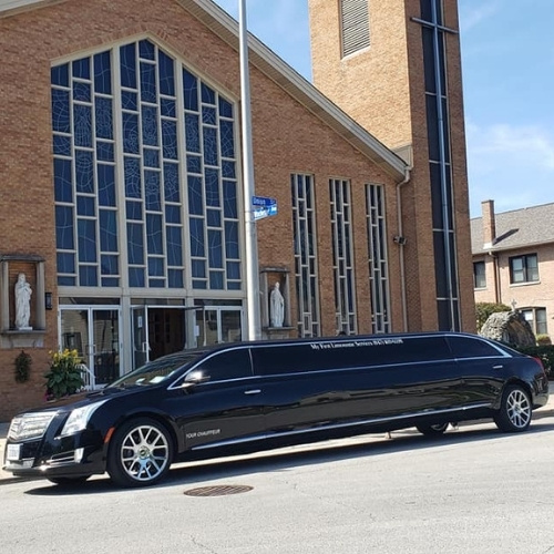 black limousine parked in front of a brick church with stained glass windows